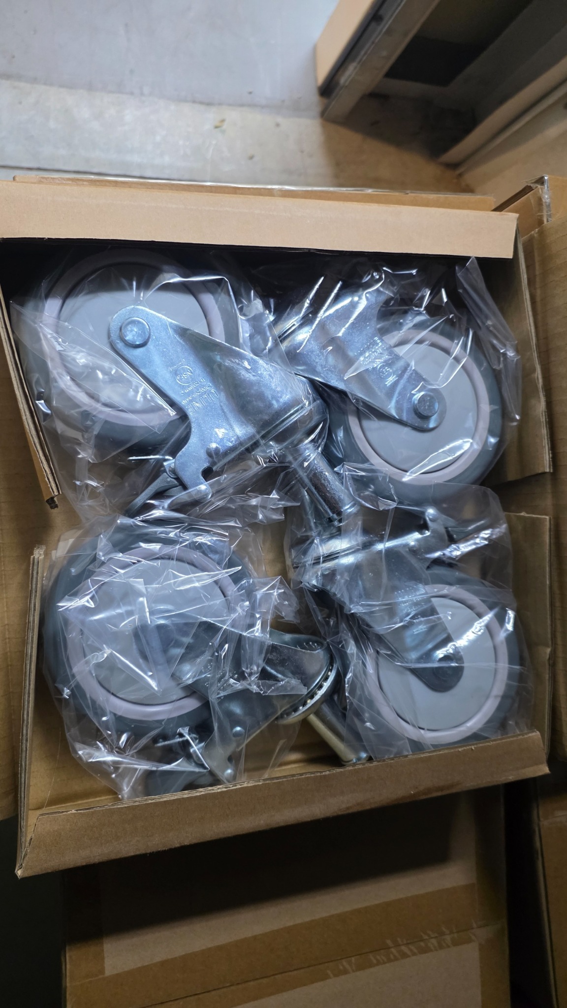 Four chrome Uline casters in plastic packaging inside an open carton